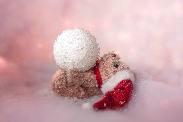 Small teddy bear in a Santa hat on his back with a snowball