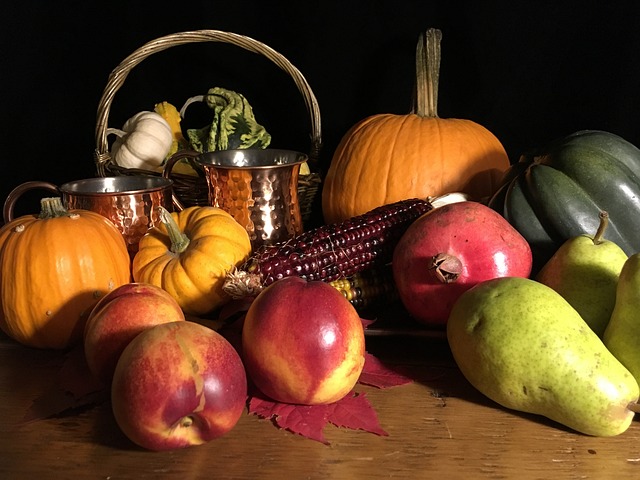 Fruits and vegetables on a table, including pumpkins, apples and nuts with a aasket in the background