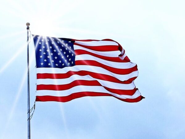 American flag lit by white sunlight as it waves against a blue sky