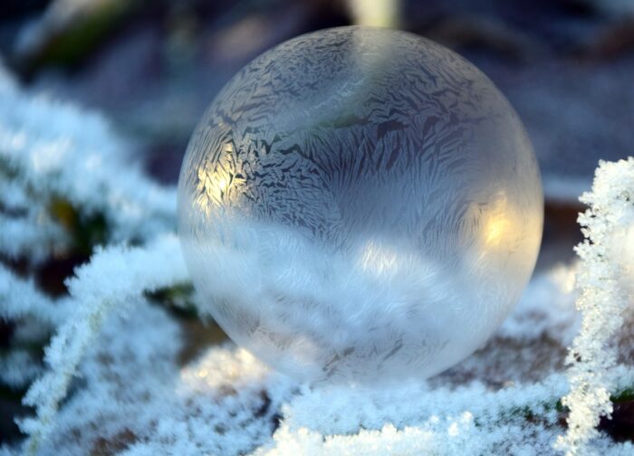 Frozen soap bubble sits amid snow in an outdoor setting with gold lights in the background.