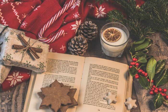Book open with eggnog nearby, Christmas gingerbread stars set on its pages and surrounded by pinecones holly and a candy cane.