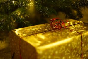 Christmas package in gold foil wrap with curled red ribbon under a Christmas tree