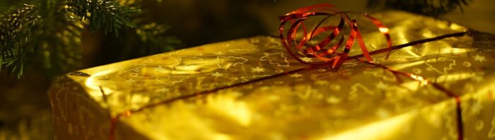 Christmas package in gold foil wrap with curled red ribbon under a Christmas tree