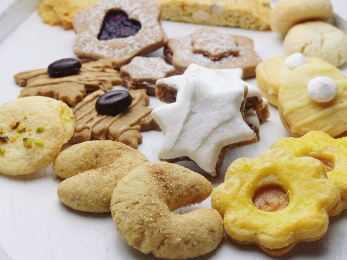 Assortment of Christmas cookies on a table, including a six-pointed star with white icing, crescent-shaped cookies and cutout cookies with a heart shape in the center filled with raspberry jam