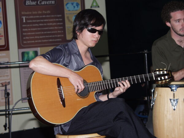 Guitarist Dat Nguyen wears dark glasses as he plays onstage.