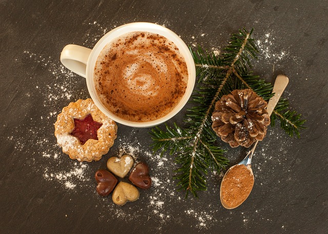 Hot cocoa mug sits near a pinecone and a spoon filled with chocolate powder near two Christmas cookies