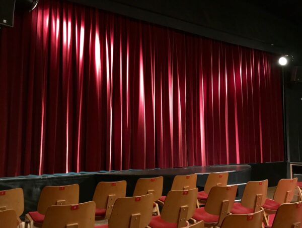 Wooden chairs in front of a stage with a lowered red curtain
