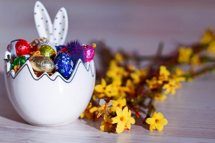 Easter basket in the shape of a white ceramic hatched egg, filled with chocolate eggs and with rabbit ears