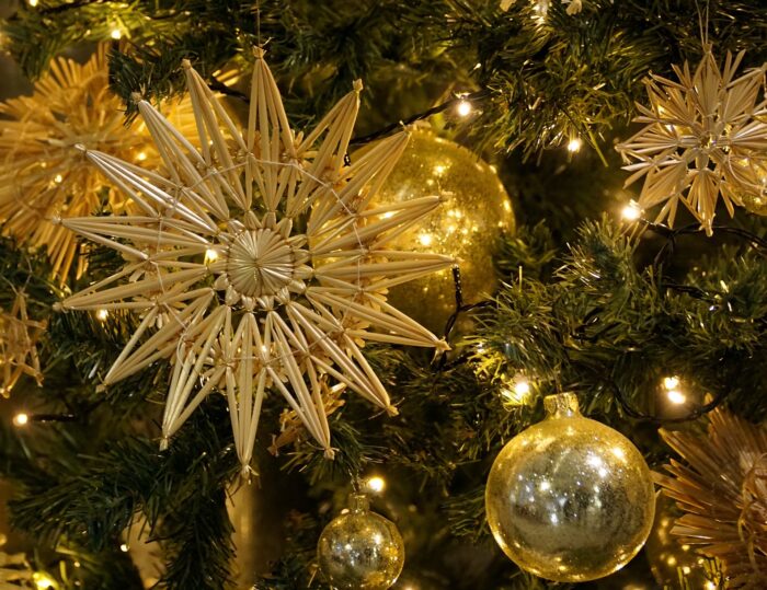 White lights sparkle behind gold Christmas star and gold ornaments on pine branches, in closeup.