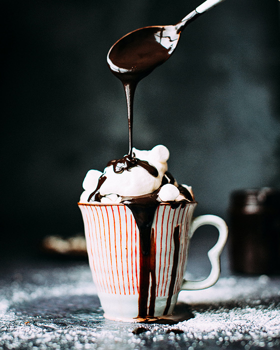 Chocolate sauce getz drizzled on whipped cream in a white cup with red stripes and a heartshaped handle.
