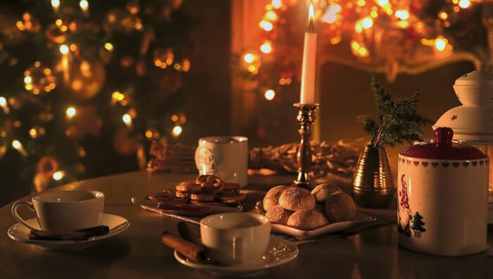 Christmas table set with a white candle, coffee cups and cookies with strings of white lights in the background.