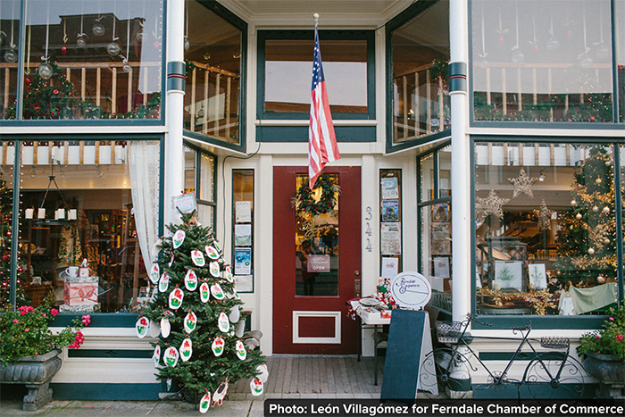 Old-fashioned shop windows on either side of a wooden door festooned with a wreath and displaying the American flag