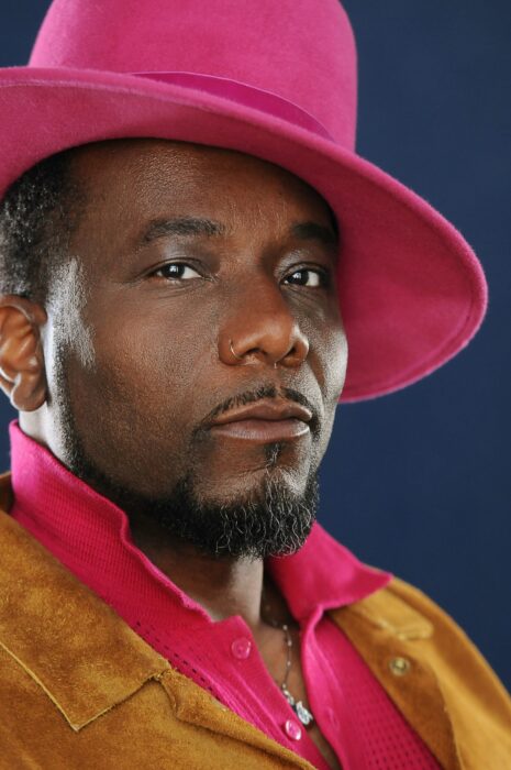 Closeup of Martin LUther McCoy, in a suede jacket with a hot-pink shirt and hat.