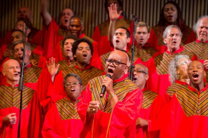 GLIDE Ensemble and Change Band, in red choir robes with gold trim, singing.