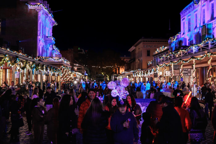Shoppers crowd the street outside lighted Old Sacramento Waterfront buildings lit up for Christmas.