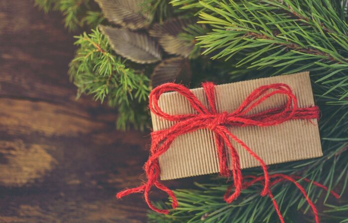 Package wrapped in brown corrugated paper and tied with red yarn on a pine branch.