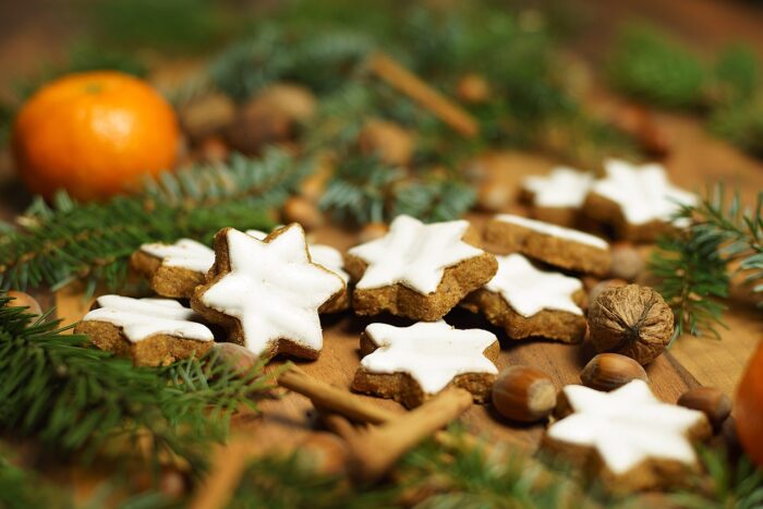Iced gingerbread stars near cinnamon sticks and an orange.