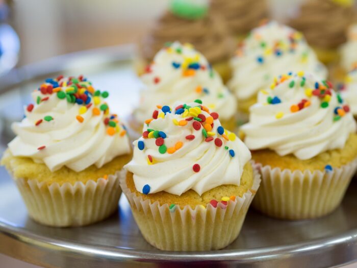 Yellow mini-cupcakes with white icing and rainbow sprinkles on a plate.