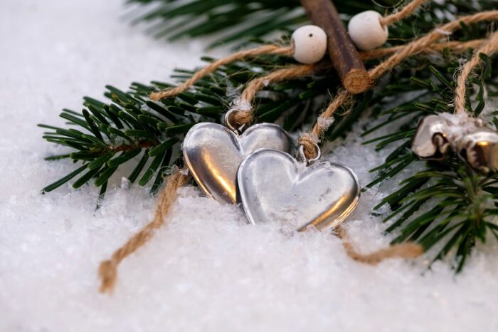 Two gold hearts with silver highlights tied to a pine branch with twine against snow