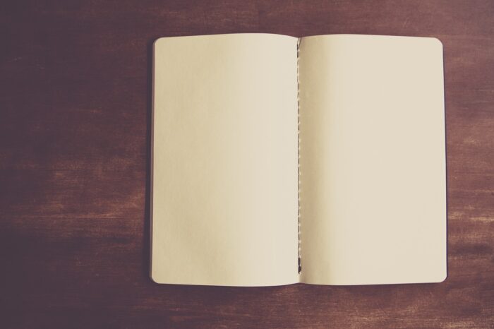 Blank book sits open with cream-colored pages against a wood background.
