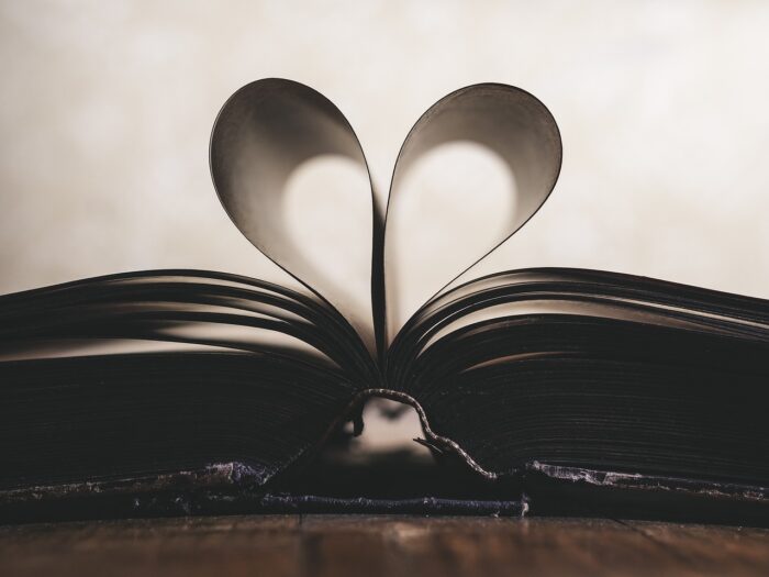 Two pages of an open book curl towards each other to form a heart.