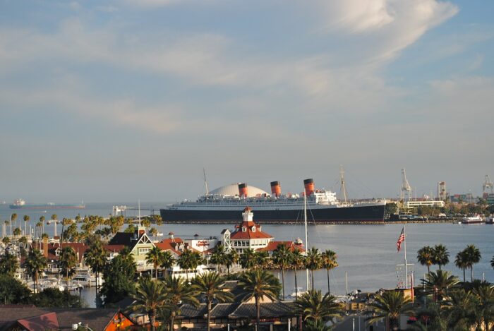 Queen Mary sits in the harbor with Shoreline Village shops in the foreground.