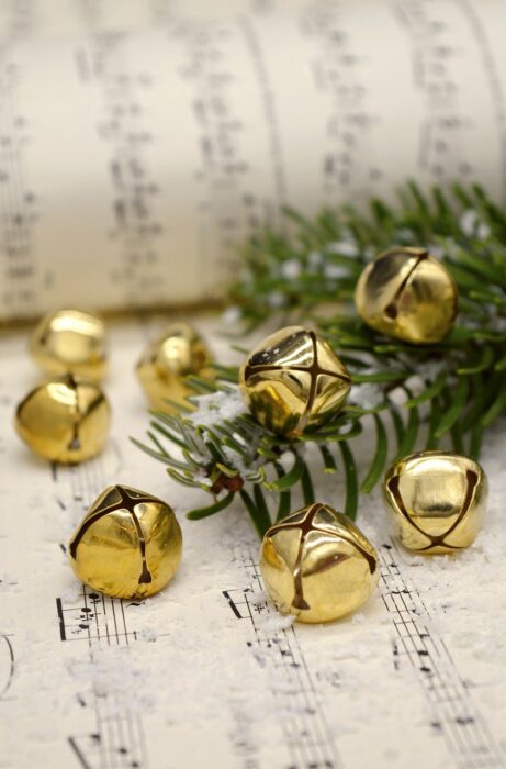 Musical score with a pine branch and gold jingle bells on top of it.