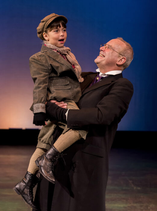 Geoff Elliott, as Scrooge, lifts Tiny Tim, played by aNNALISE moRRIS.