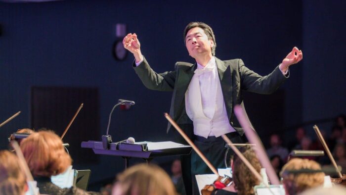 Jun-Ho Pak, with baton, conducts Philharmonic violinists