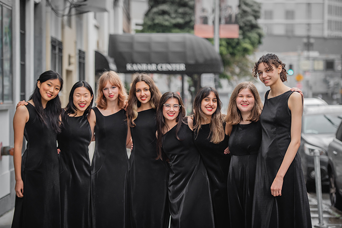 Seven young girls, in black satin sleeveless gowns, smile against a San Francisco street background.