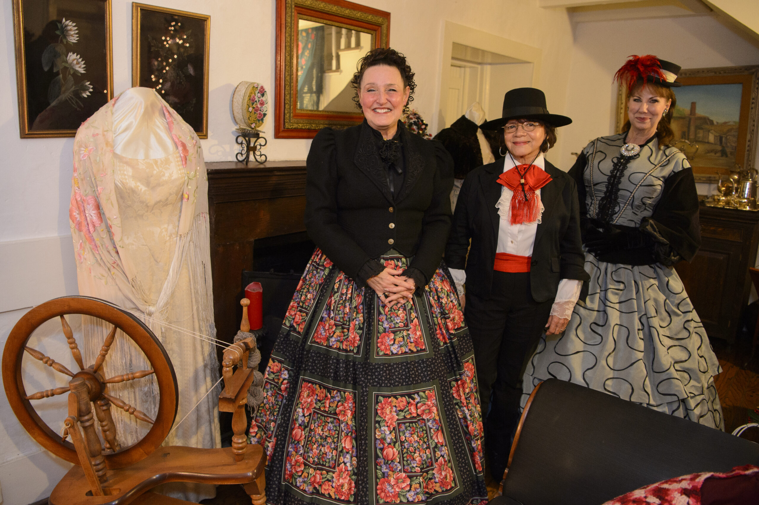 Three volunteers in traditional Mexican costume, welcoming guests next to an antique spinning wheel.