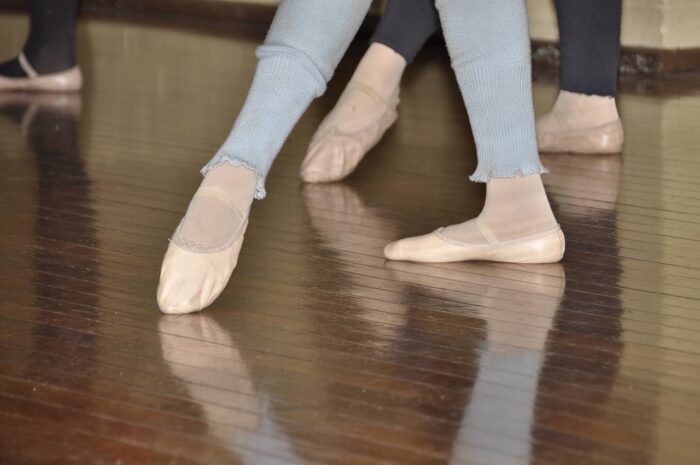 Two dancers' legs and feet as they point their toes in pink ballet shoes. Dancers are wearing jeans and slacks.