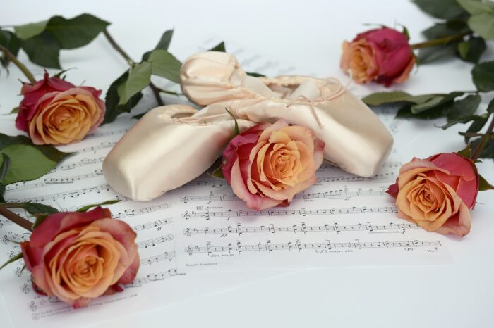 Pink satin ballet shoes on a musical score, sourrounded by pink roses