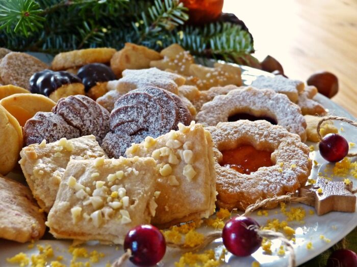 Plate of Christmas cookies: includes butter cookies, jam thumbprint and chocolate snowballs, near Christmas greenery,.