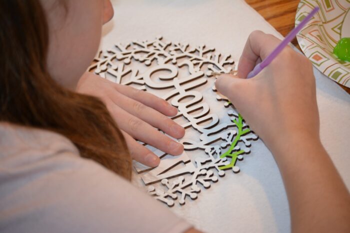 Young woman stencils a filigree paper design with "Happy" visible in a wreath.