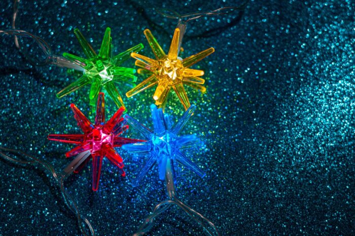 Red-yellow, blue and gren Christmas lights sparkle against a dark-green background.