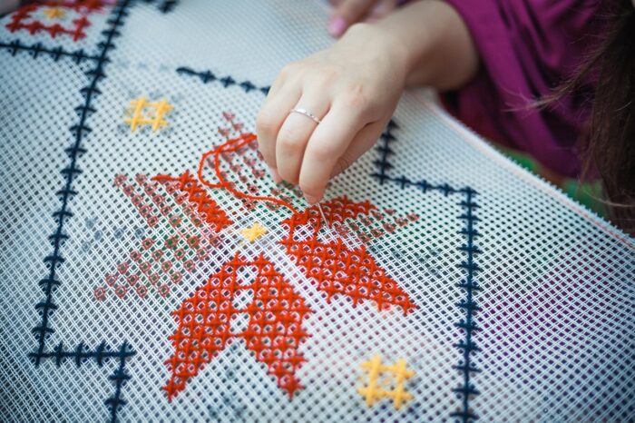 Woman's hand closeup as she stitches an eight-pointed star on a needlework canvas.