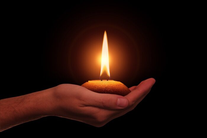 Hand extends a small candle in darkness