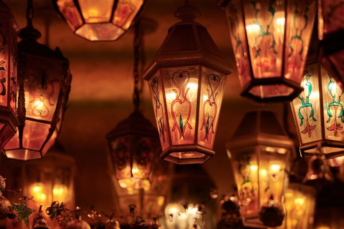 Seven lighted lanterns cast an amber glow as they hang from a ceiling