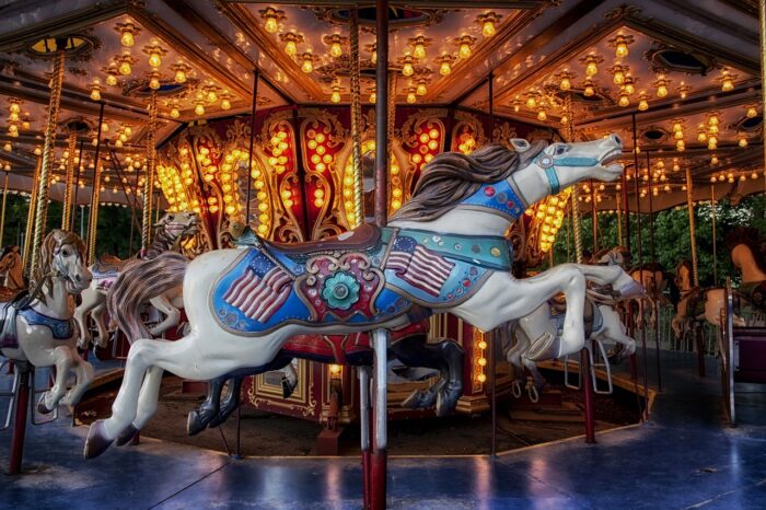 Carved white wooden carousel horse decorated with two American flags on a lighted carousel.