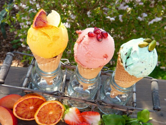 Three ice cram cones in a carrier: orange, pink and green ice cream scoops