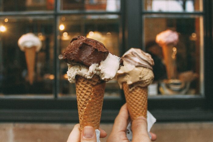 Two hands hold ice-cream cones of chocolate, fudge ripple and vanilla together