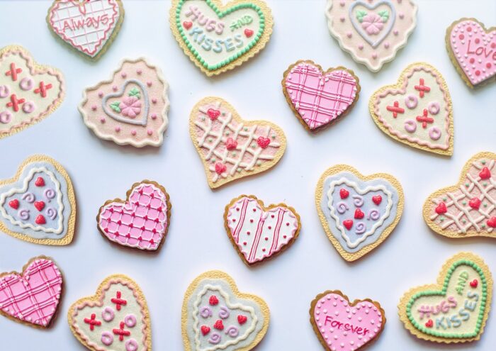 Valentine sugar cookies with pink, white and pastel green icing and red hearts, on a blue surface.