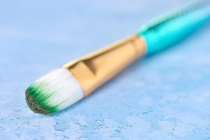 White paintbrush with green paint on the bristles and a turquoise handle, on a light-blue background.