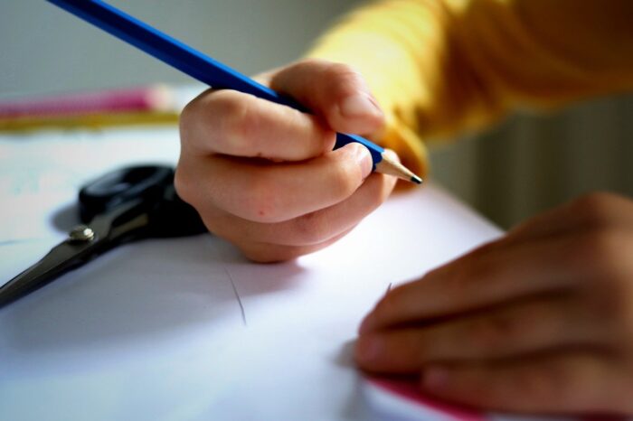 Child's hands hold pencil over a blank sheet of paper