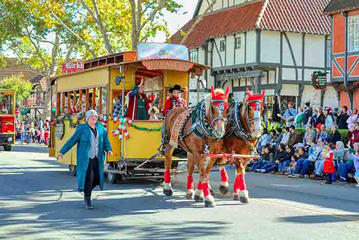 Horses with red plumes pull a greenery-trimmed trolley down Solvang's main street in the Julefest parade.