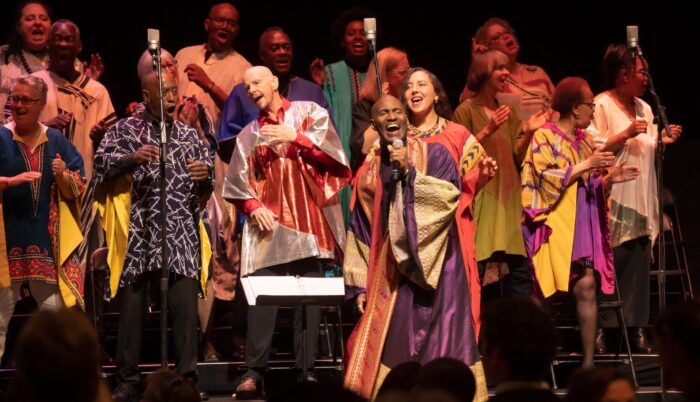 GLIDE Ensemble, in red, gold and white choir robes, singing onstage.