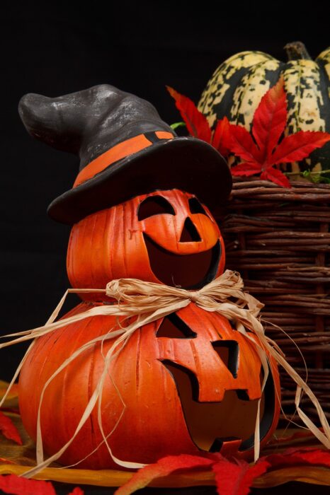 Two grinning jack-o-lanterns, with a smaller one wearing a witch's hat stacked atop a larger one