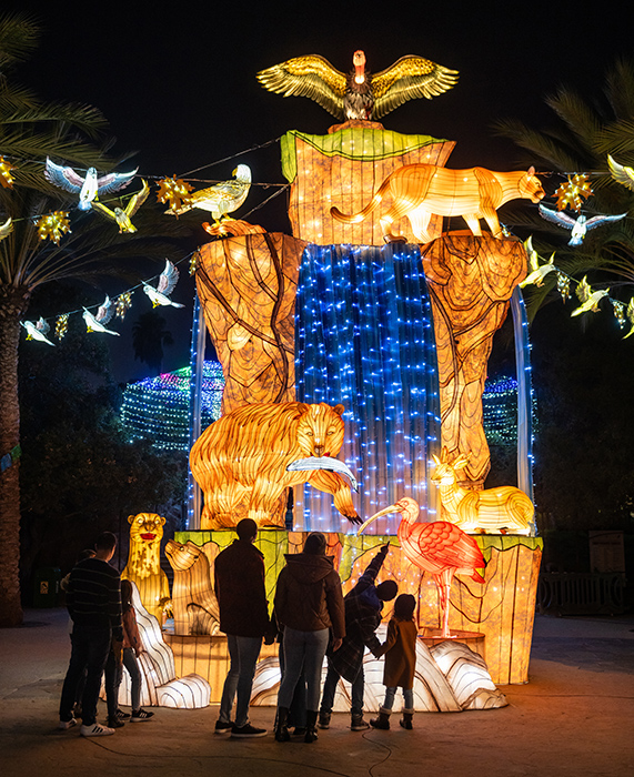 Attendees stop by a lighted sculpture of tigers, a mountain lion, a deer and a bear with a fish in its mouth, with white doves flying overhead