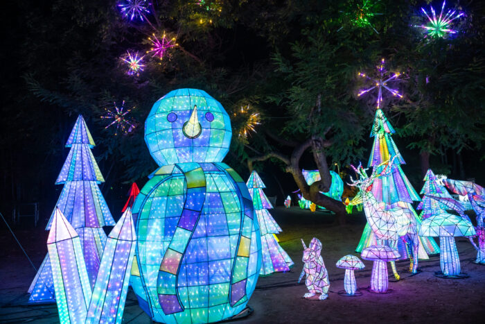 Lighted sculptures of a giant snowman, deer and rabbit among pine trees